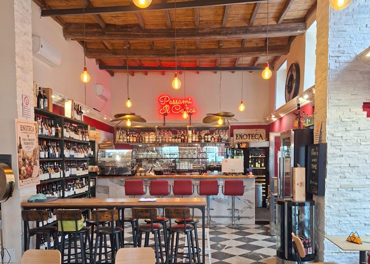 La parete dell'enoteca con la selezione di bottiglie e il tavolo alto con gli sgabelli